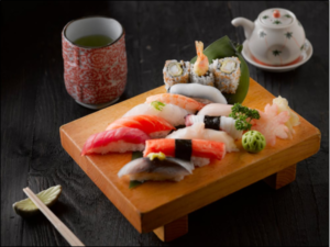 Fresh sushi and sashimi platter with maki rolls served on wooden board alongside green tea in traditional Japanese setting.