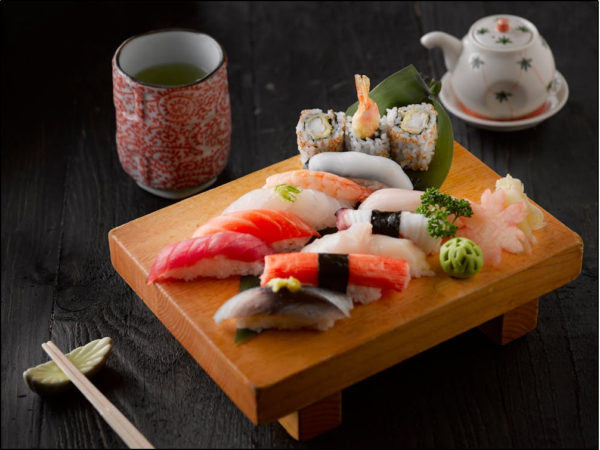 Fresh sushi and sashimi platter with maki rolls served on wooden board alongside green tea in traditional Japanese setting.