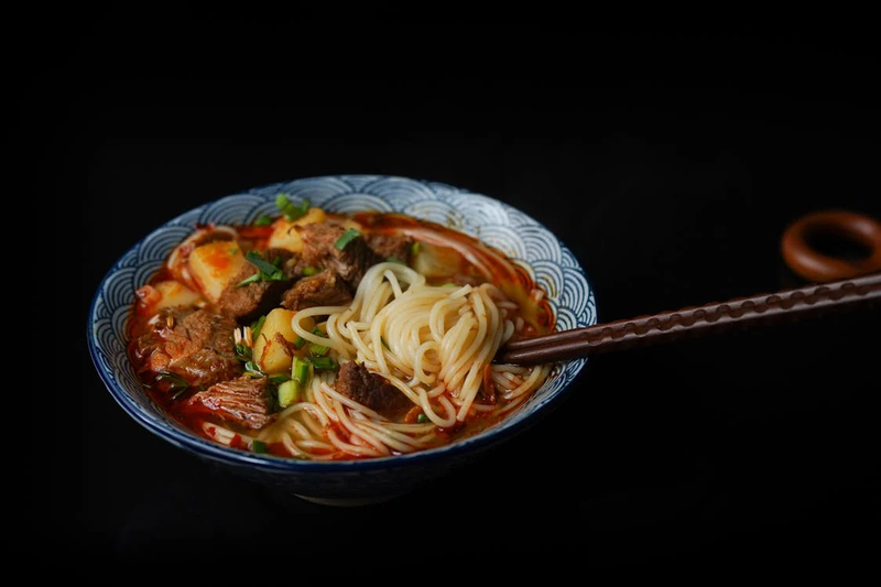 Steaming bowl of shoyu ramen with thin noodles, sliced pork, bamboo shoots, and green onions in clear golden broth