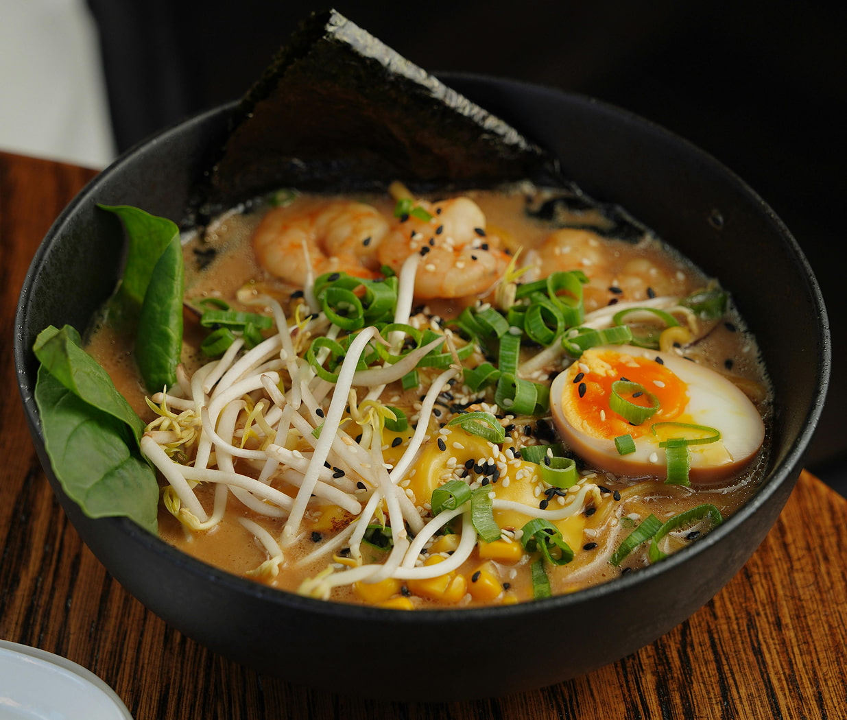 A bowl of miso ramen soup with fresh noodles, soft-boiled egg, shrimp, bean sprouts, corn, scallions, and seaweed.